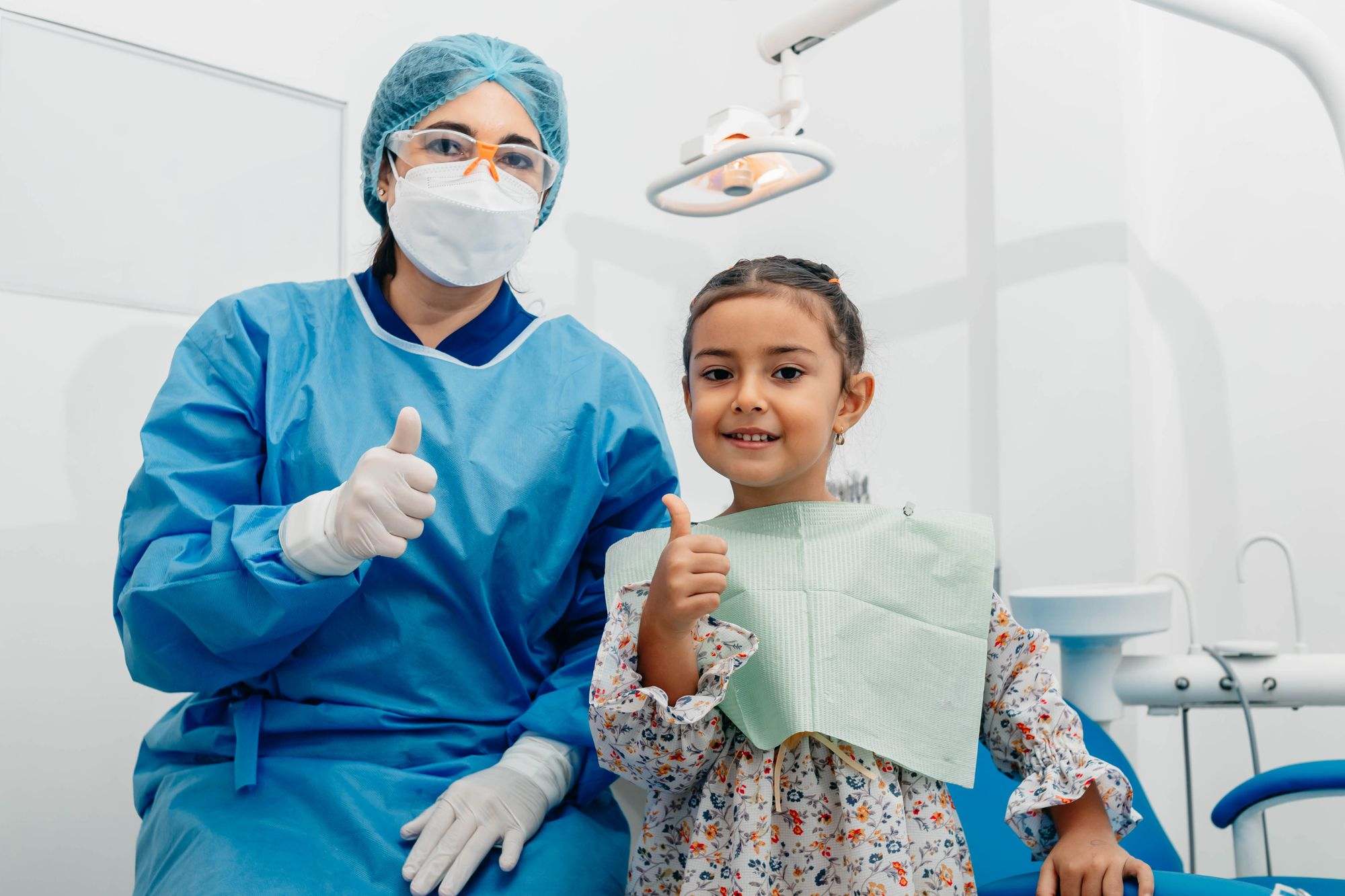 Una dentista y una niña levantan el pulgar en el consultorio